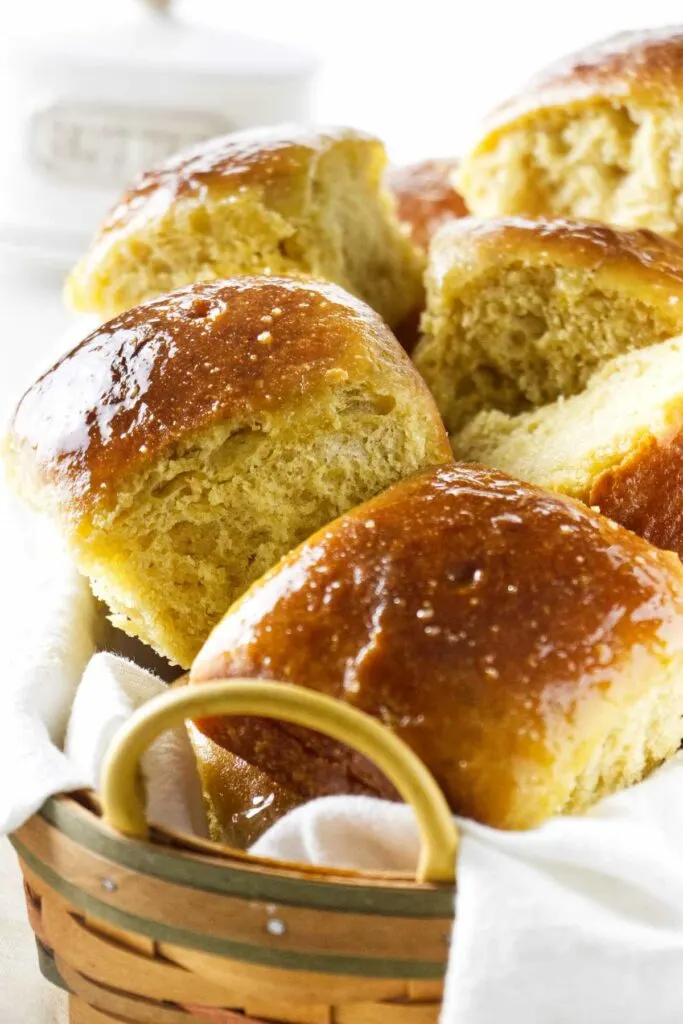 Bread rolls in a basket with a tray of butter in the background.