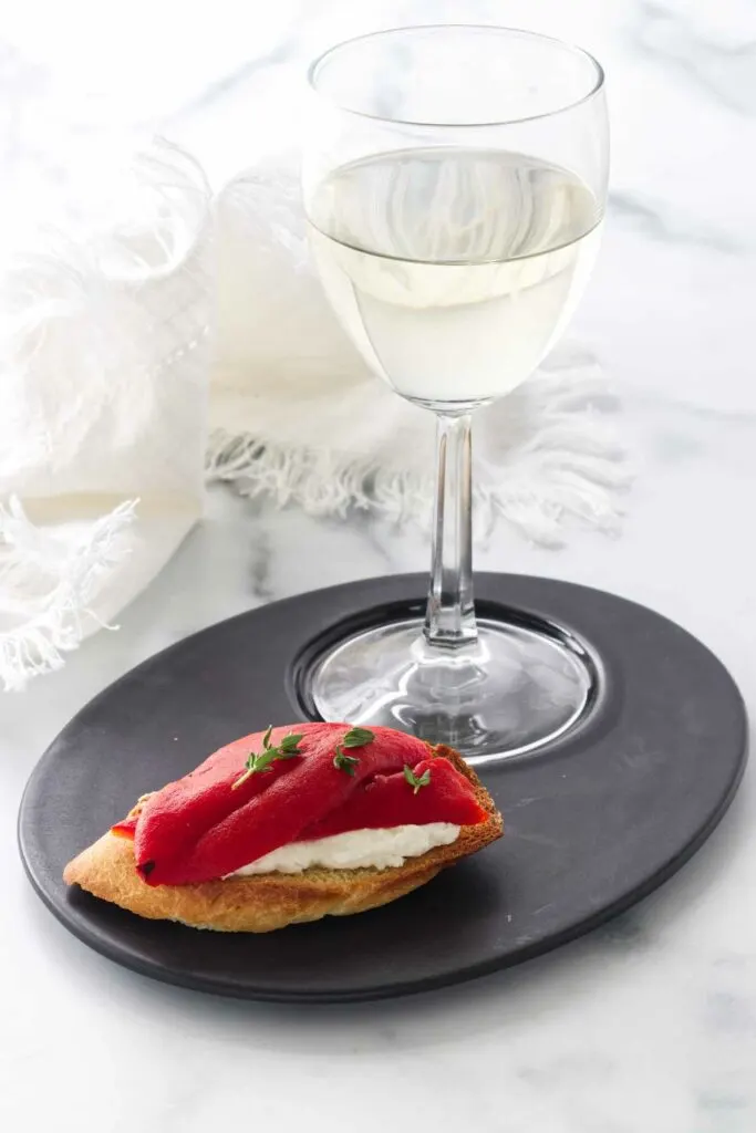 A bruschetta on a plate with a glass of wine.