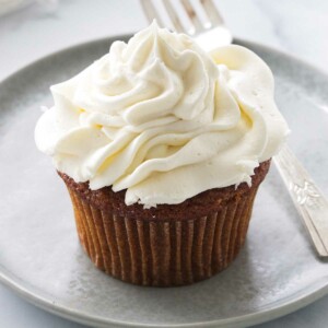 A serving of a frosted cupcake on a plate with a fork.