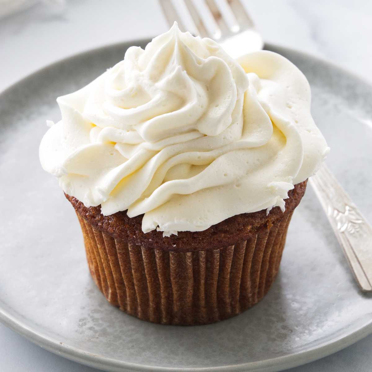 A serving of a frosted cupcake on a plate with a fork.