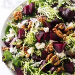 A salad bowl filled with greens, roasted beets, blue cheese, and walnuts.