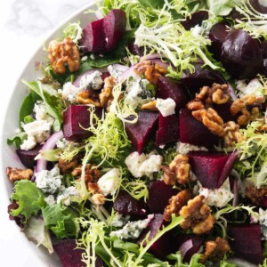 A salad bowl filled with greens, roasted beets, blue cheese, and walnuts.