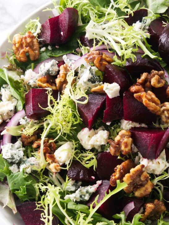A salad bowl filled with greens, roasted beets, blue cheese, and walnuts.