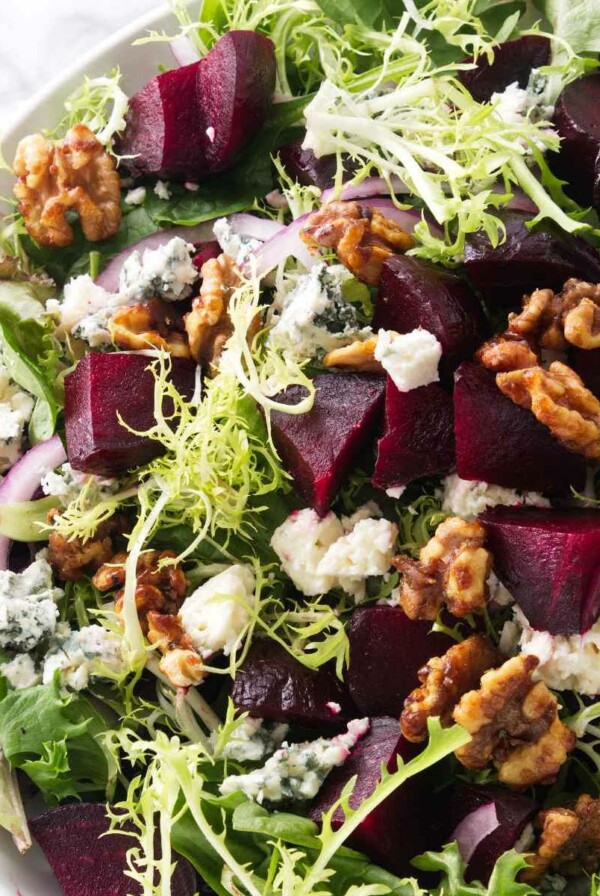 A salad bowl filled with greens, roasted beets, blue cheese, and walnuts.