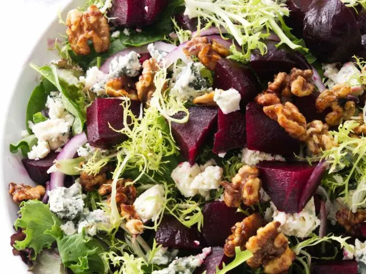 A salad bowl filled with greens, roasted beets, blue cheese, and walnuts.