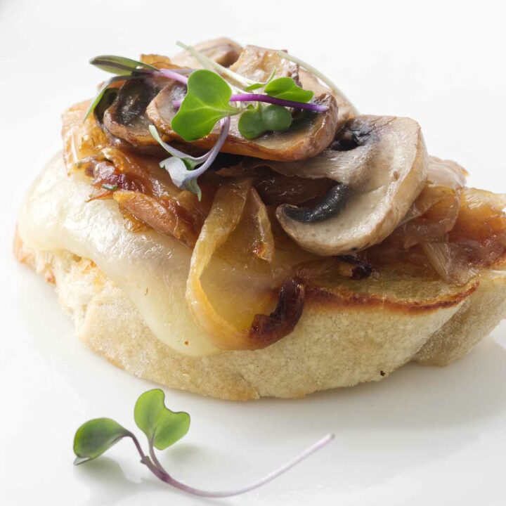 Bruschetta appetizer with caramelized onions, cheese, mushrooms and garnished with microgreens.
