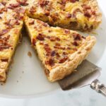 A pie lifter removing a slice of quiche from a serving plate.