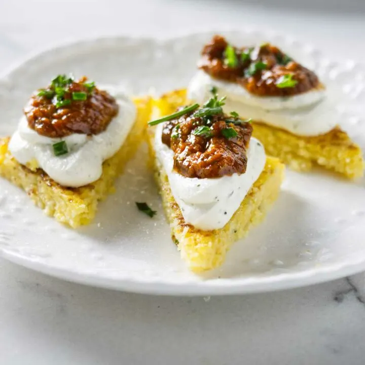 A plate of polenta bites topped with goat cheese and tomato pesto.