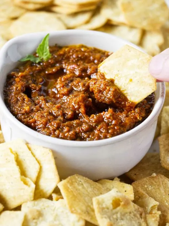 Dipping a chip into a bowl of sun dried tomato pesto.