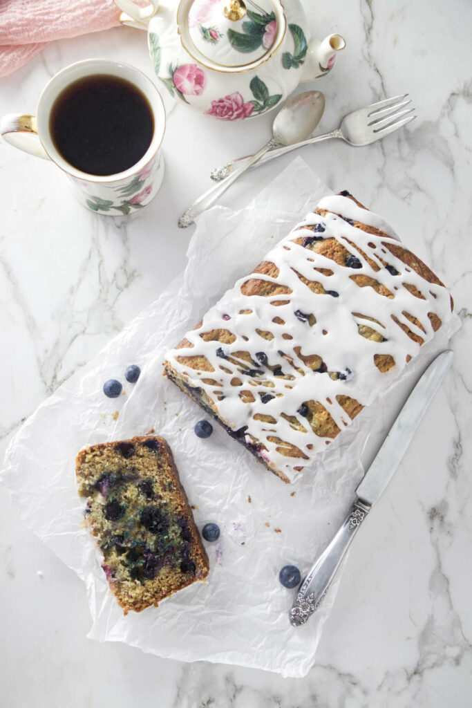 A loaf of banana blueberry bread next to a cup of coffee and a knife.