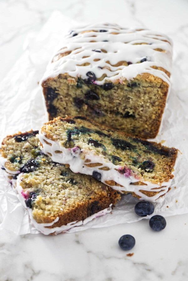 Two slices in front of a loaf of banana blueberry bread.