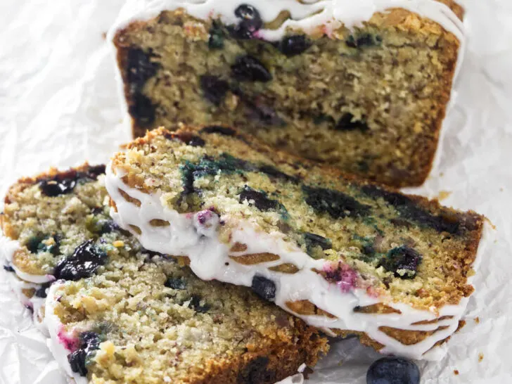 Two slices in front of a loaf of banana blueberry bread.