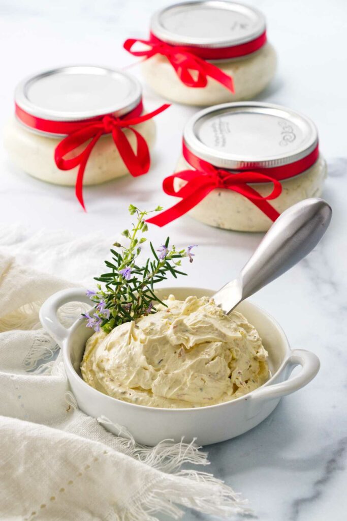 A dish of butter mixture with an appetizer knife. Three gift wrapped jars of butter mixture in the background.