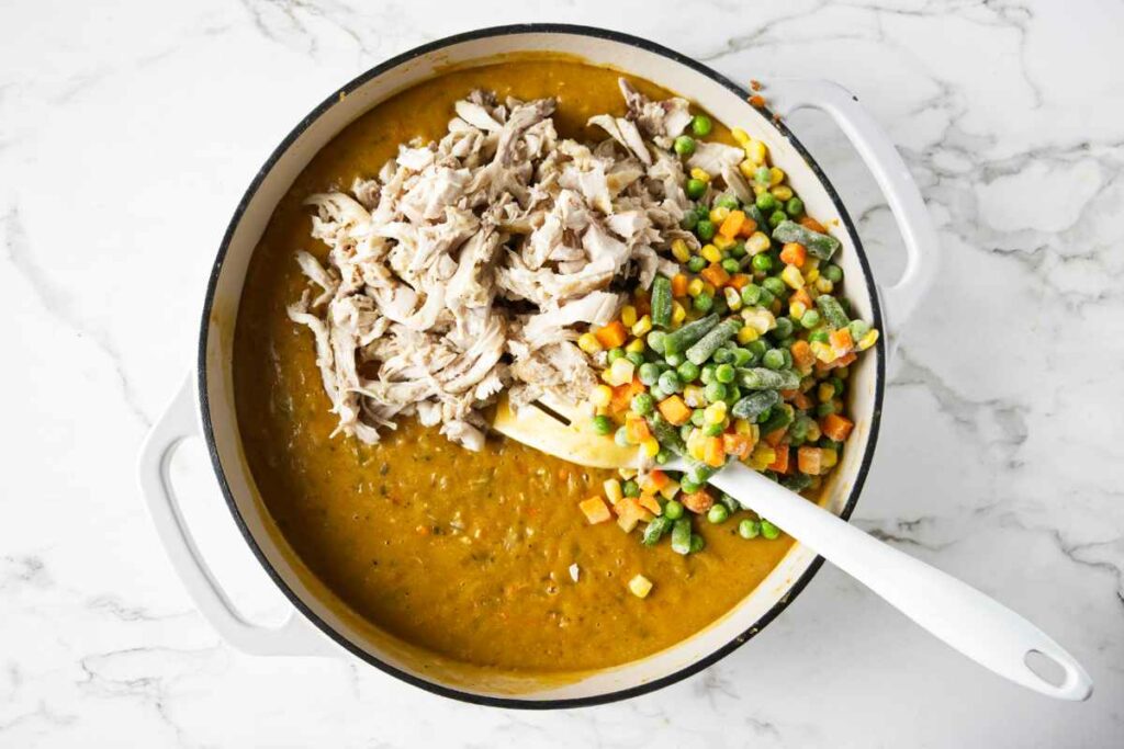 Tossing in shredded chicken and frozen veggies to a pan with sauce.
