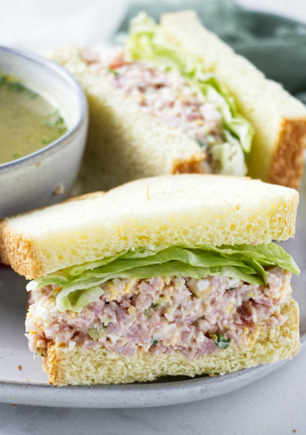 A ham salad sandwich next to a bowl of soup.