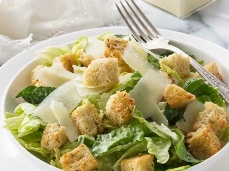 A salad bowl filled with Caesar salad and topped with homemade croutons.