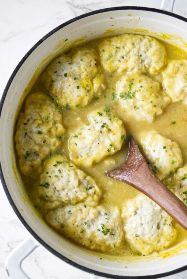 A spoon in a pot of soup with dumplings on top.