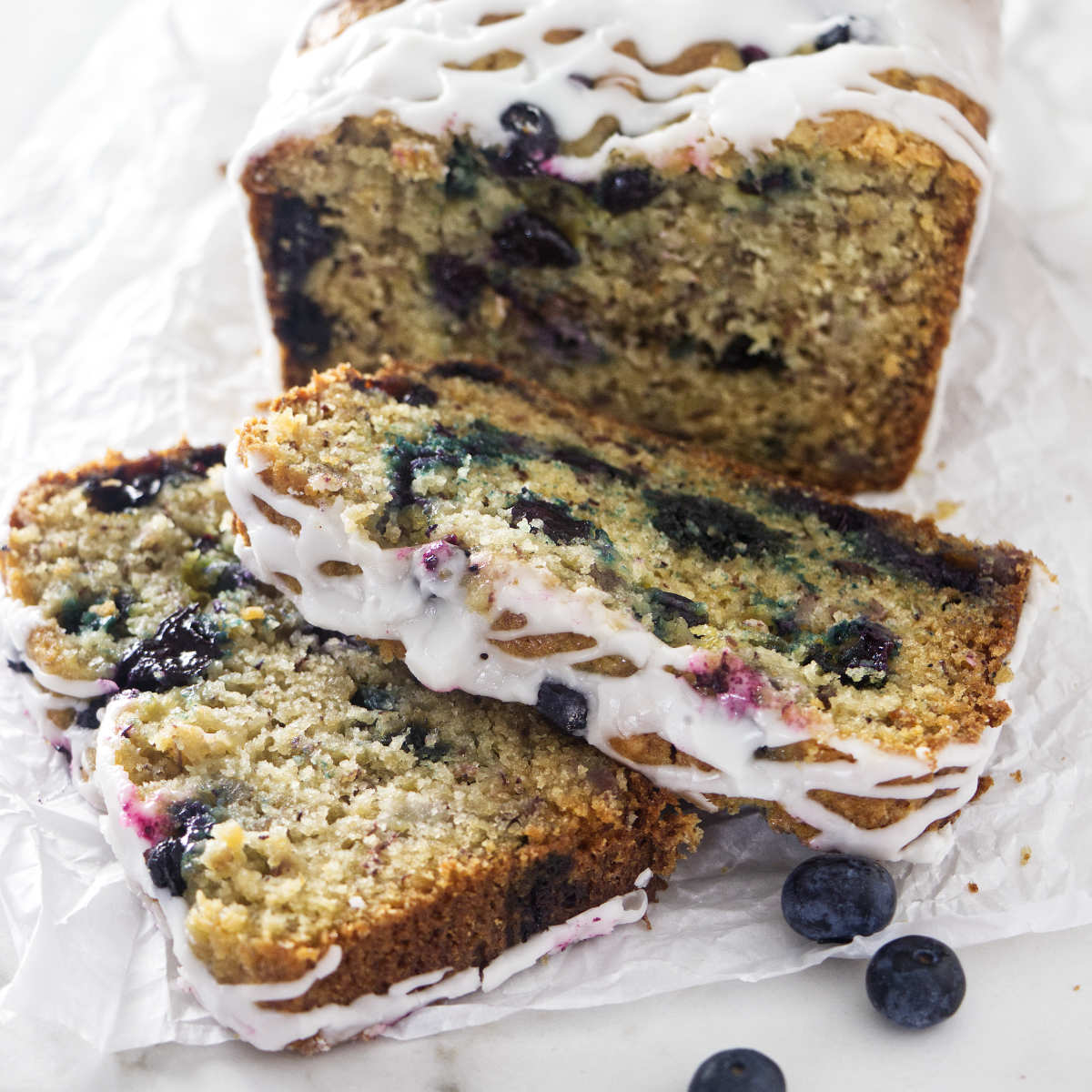 Slices of banana bread with blueberries on white parchment paper.