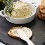 An appetizer knife spreading bone marrow butter on a cracker. A dish of the butter in the background.