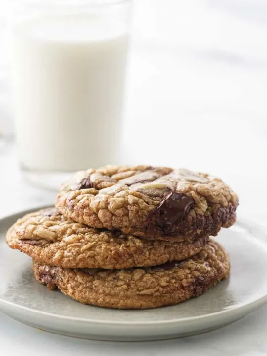A stack of chocolate chip cookies in front of a glass of milk.