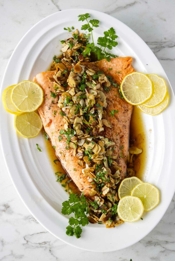 Steelhead trout amandine on a serving platter with lemon slices.