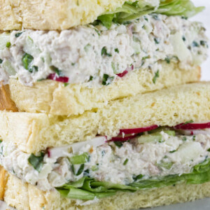 A turkey salad sandwich on white bread with lettuce and red radishes.