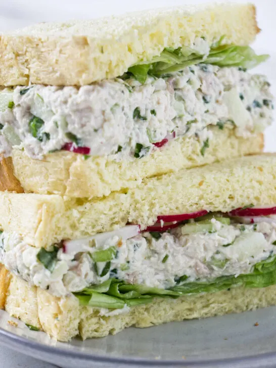A turkey salad sandwich on white bread with lettuce and red radishes.
