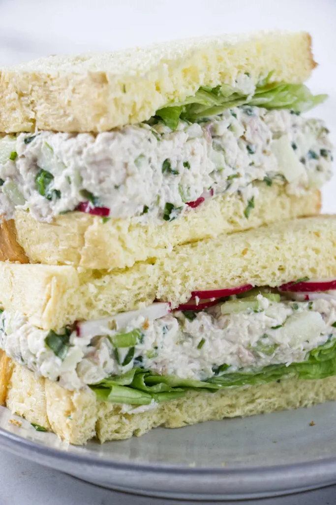 A turkey salad sandwich on white bread with lettuce and red radishes.