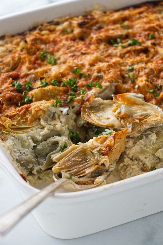 A baking dish with artichoke gratin and a spoon.