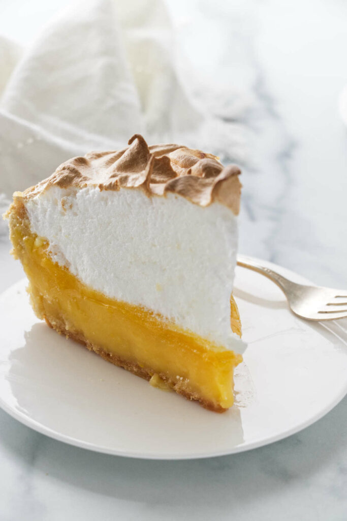 A slice of tart lemon meringue pie on a white plate.