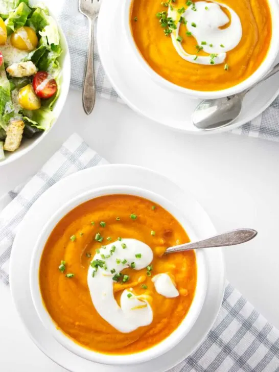Two bowls of thick carrot soup next to a salad.
