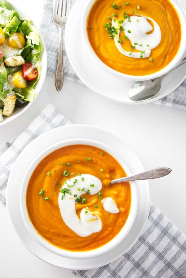 Two bowls of thick carrot soup next to a salad.