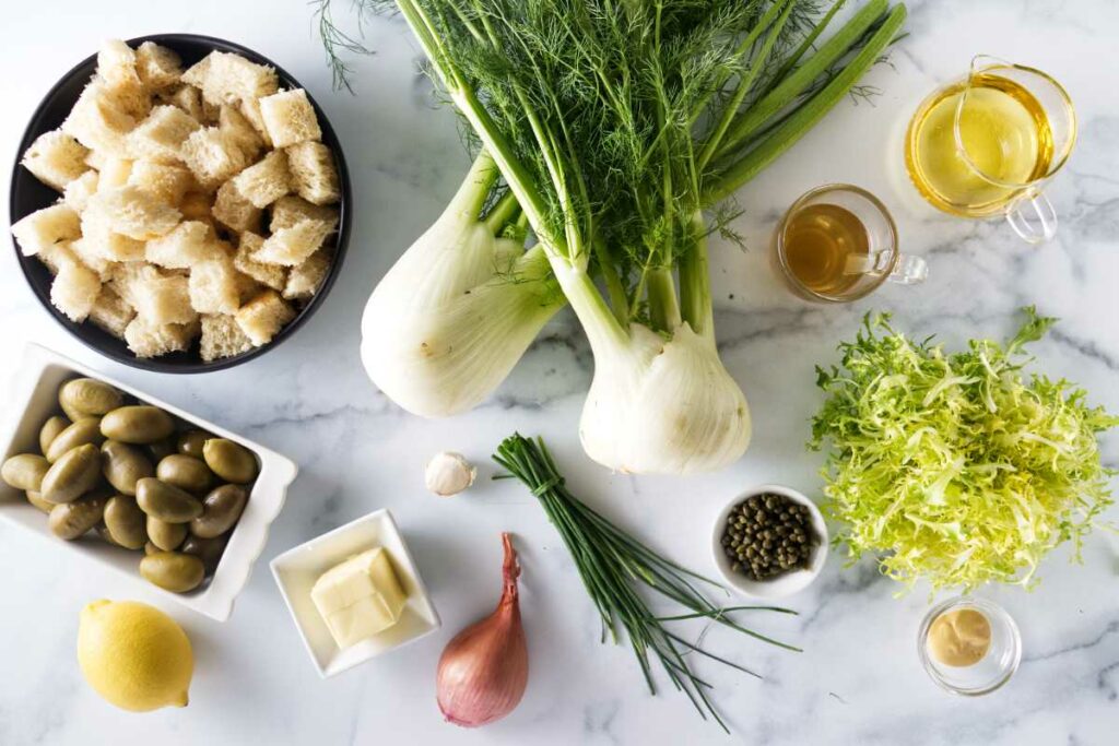 Ingredients to make a salad of fennel, croutons, green olives, capers, and lettuce.