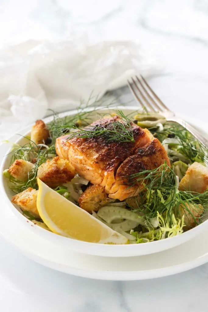 A serving of fennel salad topped with a fillet of salmon and garnished with fennel fronds.