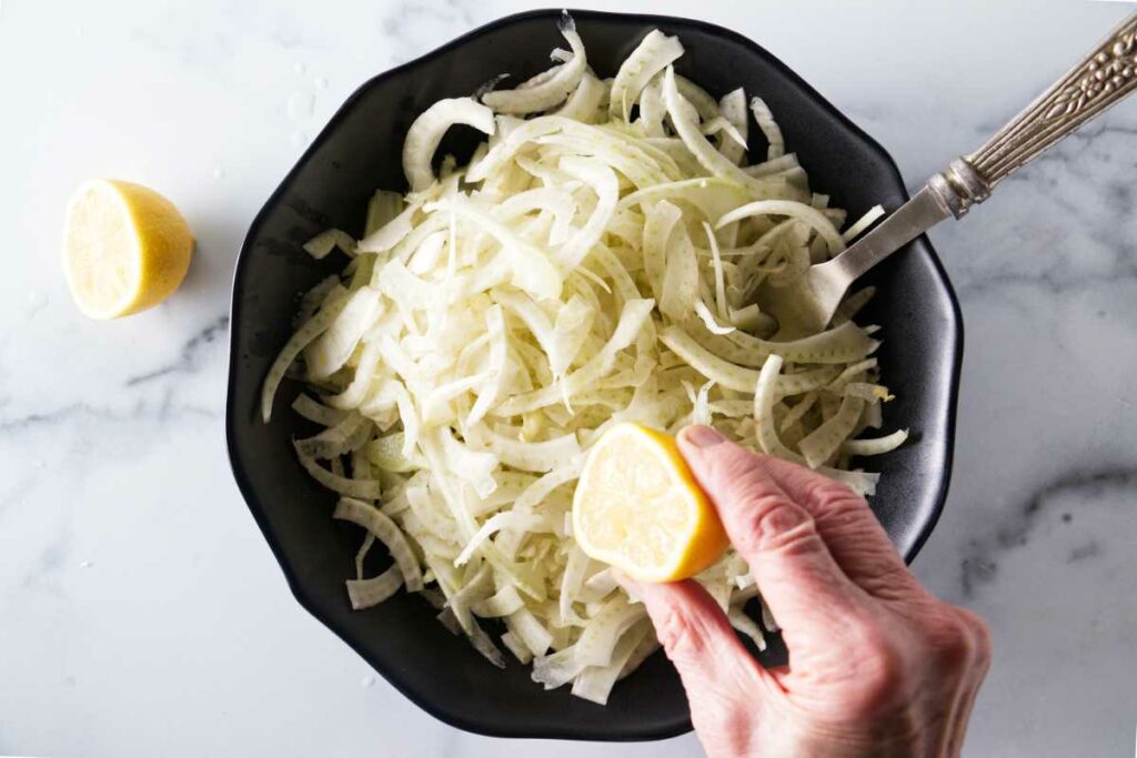 A dish with sliced fennel and a lemon being squeezed on it.