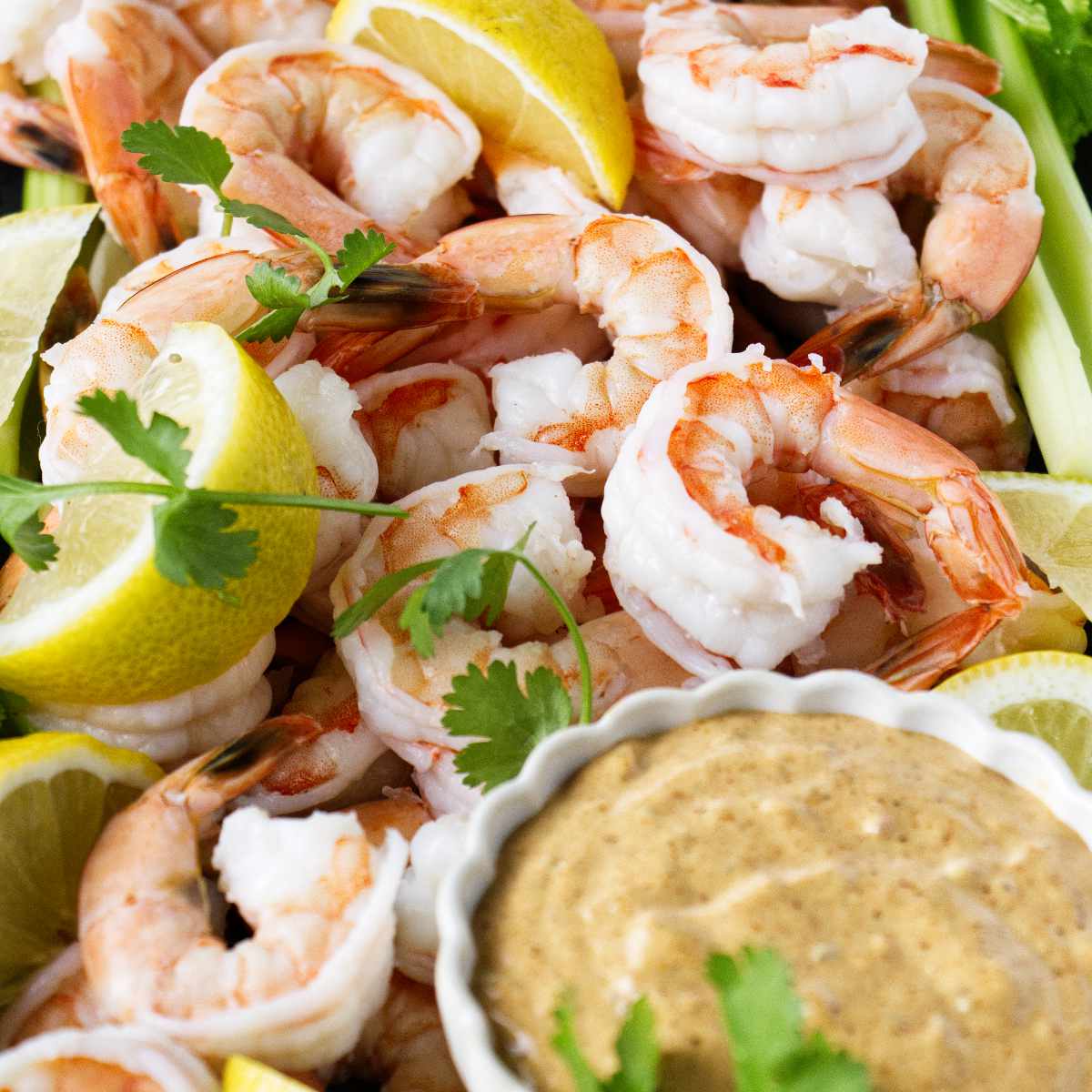 Boiled shrimp on a platter with cocktail sauce and lemon slices.