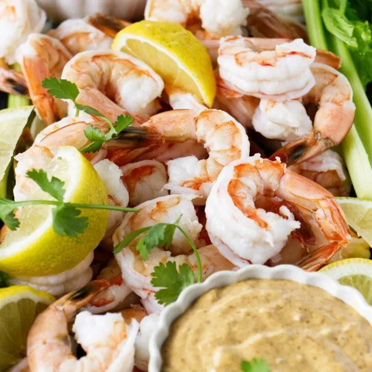 Boiled shrimp on a platter with lemon slices and cocktail sauce.