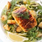 Close up view of a serving of salad topped with a fillet of salmon and garnished with fennel fronds.