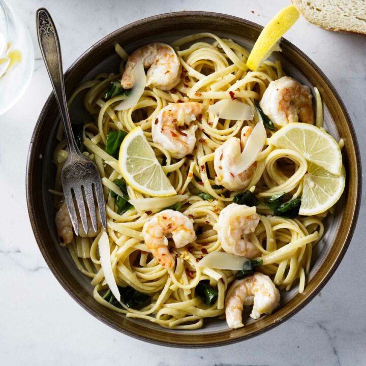 A bowl of lemon garlic shrimp pasta with slices of lemon.