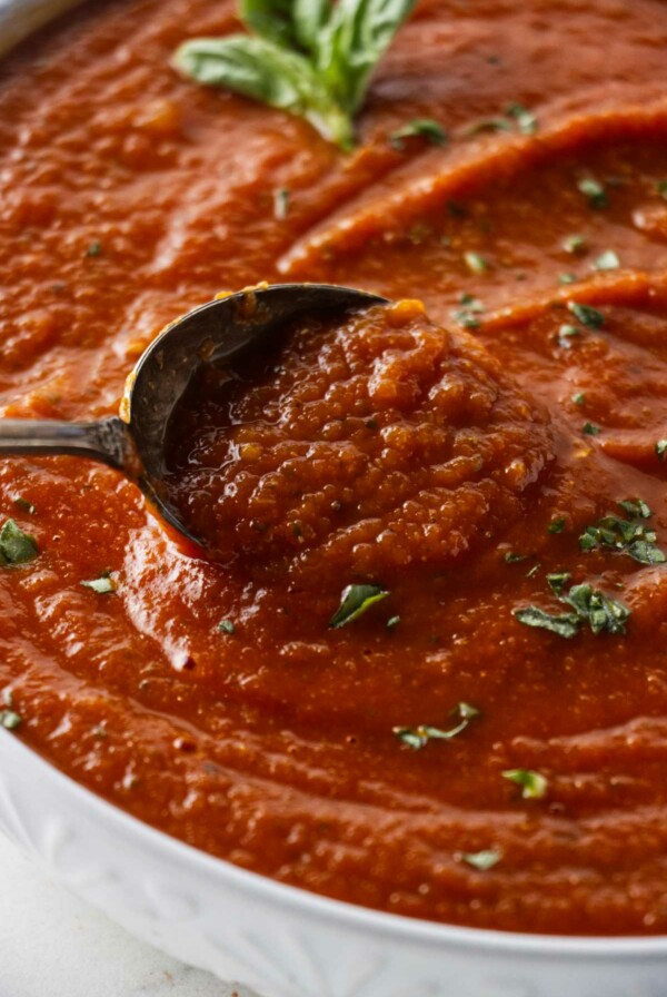 Scooping pizza sauce from a bowl.