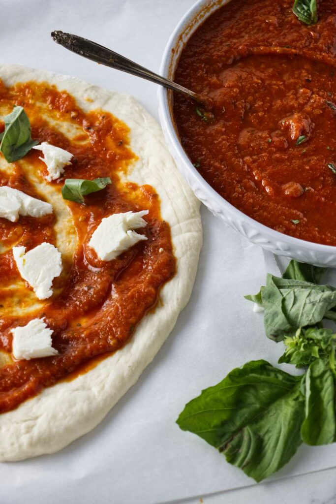 Adding pizza sauce to a round of freshly stretched pizza dough.