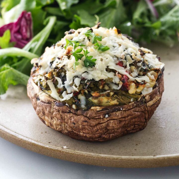 A stuffed portobello mushroom on a dinner plate with a salad.