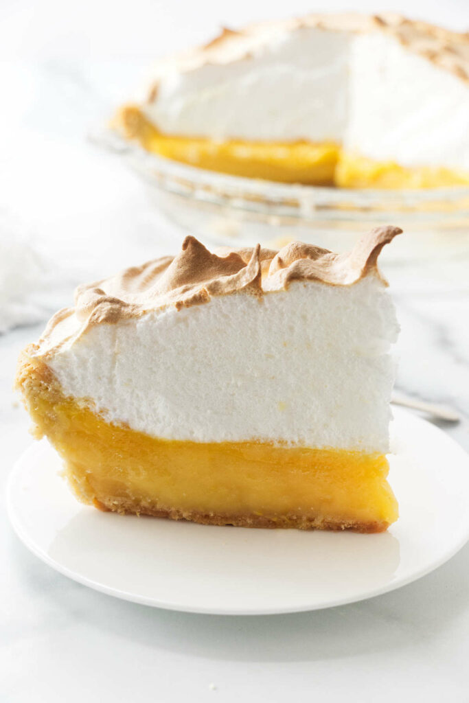 A slice of an old fashioned lemon meringue pie with a tall meringue top.