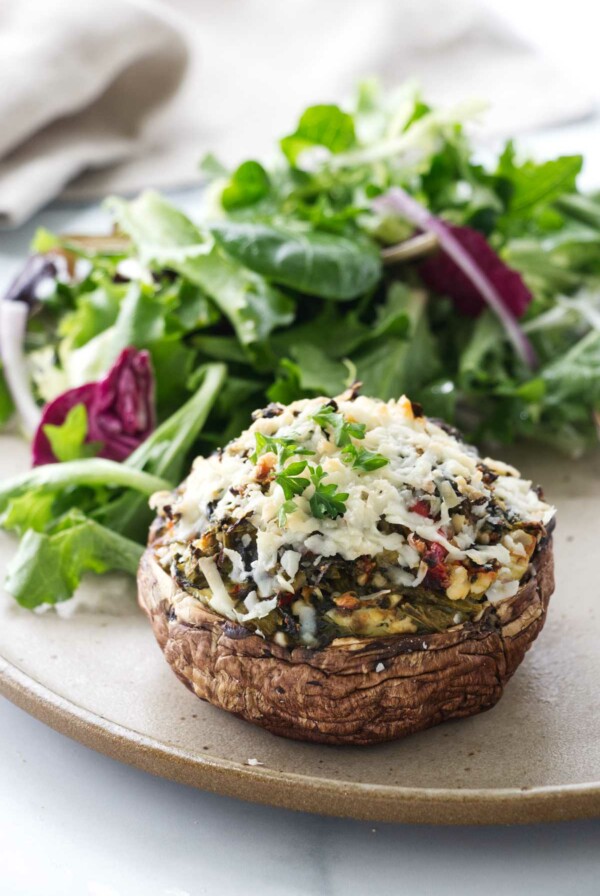 A stuffed mushroom on a dinner plate with a salad.