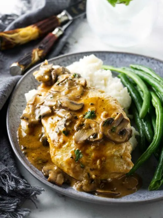 Chicken marsala on a bed of mashed potatoes next to some green beans.
