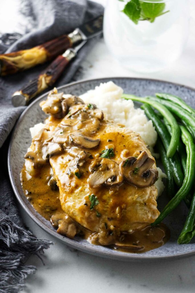 Chicken marsala on a bed of mashed potatoes next to some green beans.