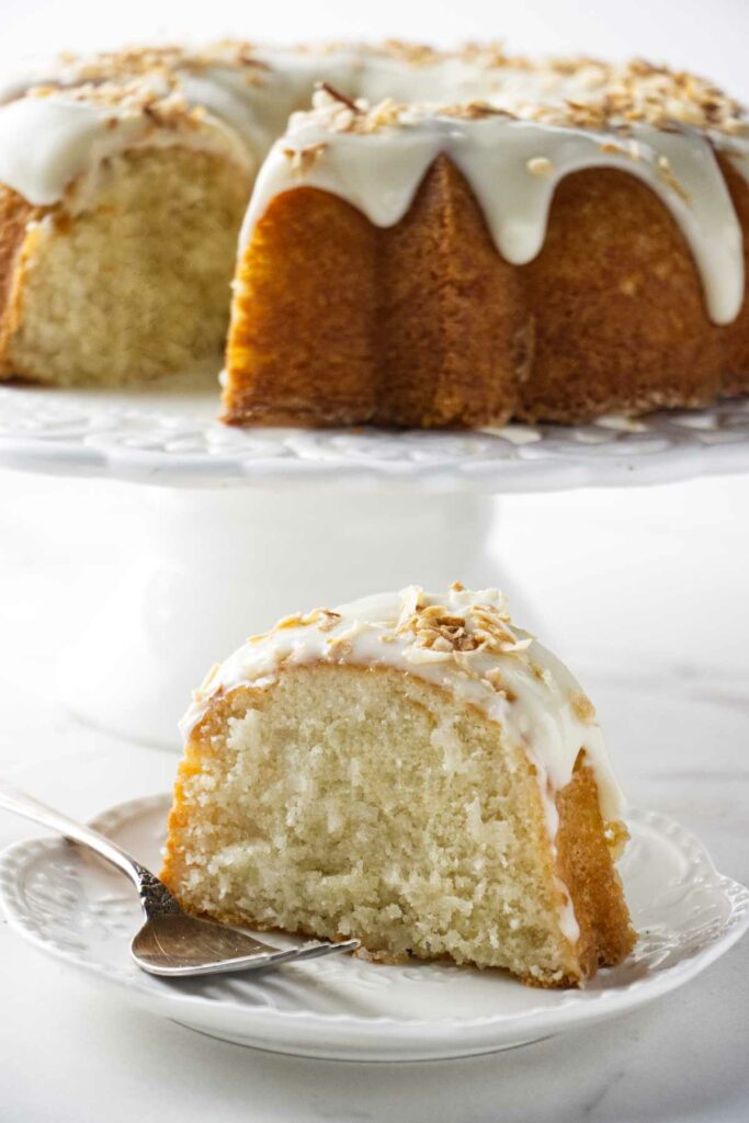 A slice of coconut cake with a larger bundt cake in the background.