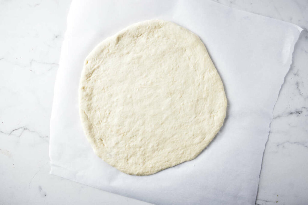 Shaping raw pizza dough on parchment paper.