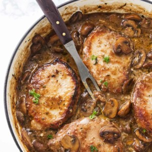 A skillet with stove top pork chop marsala and a serving fork.