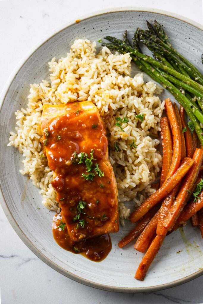 A dinner plate with marsala salmon on a bed of rice.